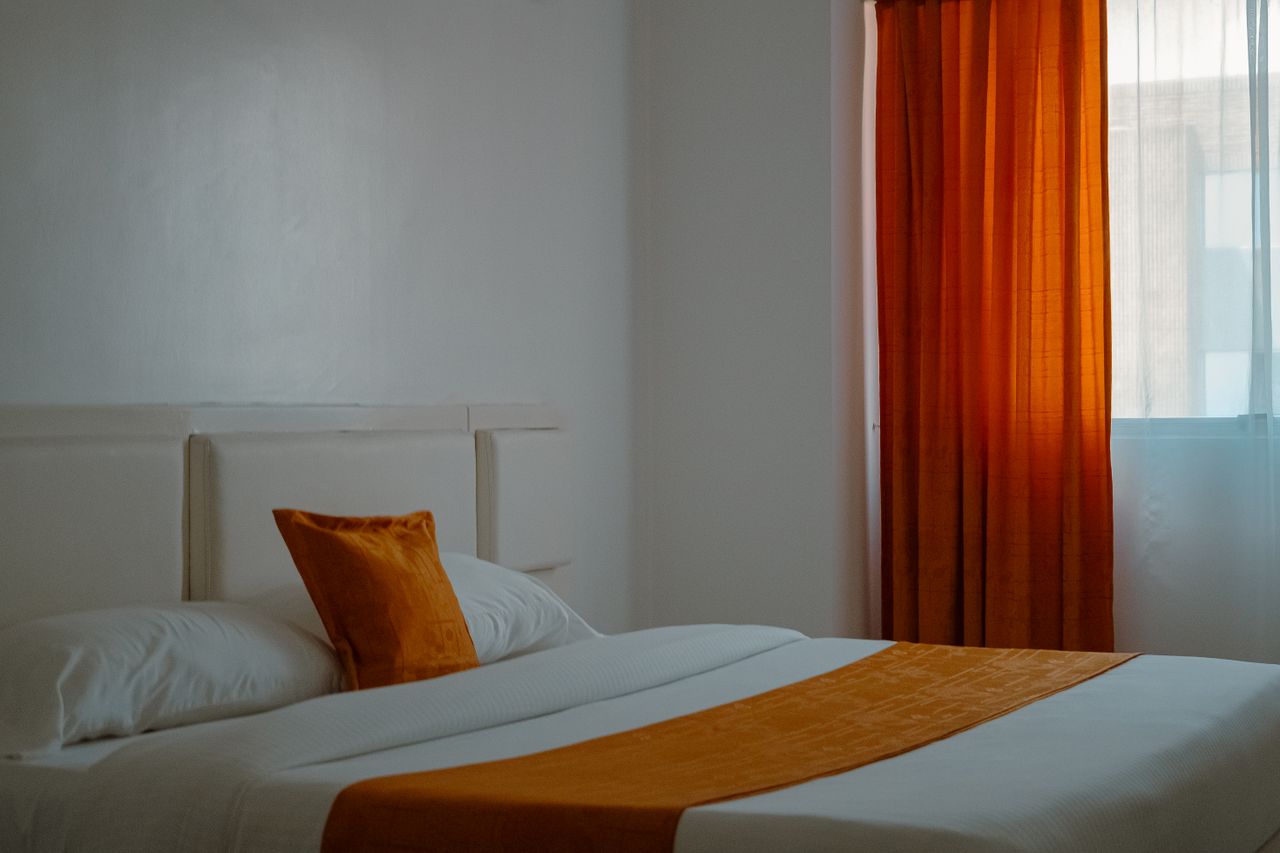 portfolio-01 Warm and inviting hotel room with orange curtains and bedding creating a cozy ambiance.